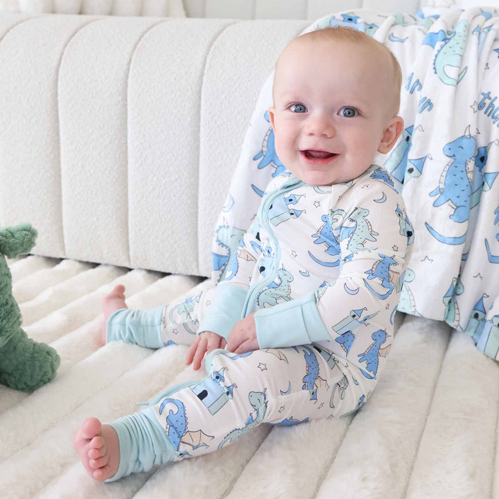 Baby in castle and dragon print romper sitting next to plush toy