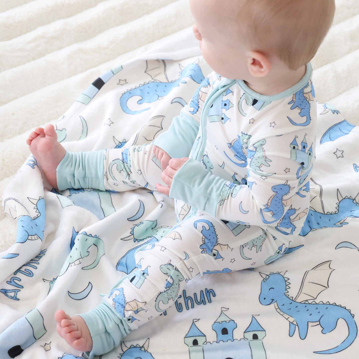 Baby sitting in long sleeve dragon romper with coordinating blanket behind
