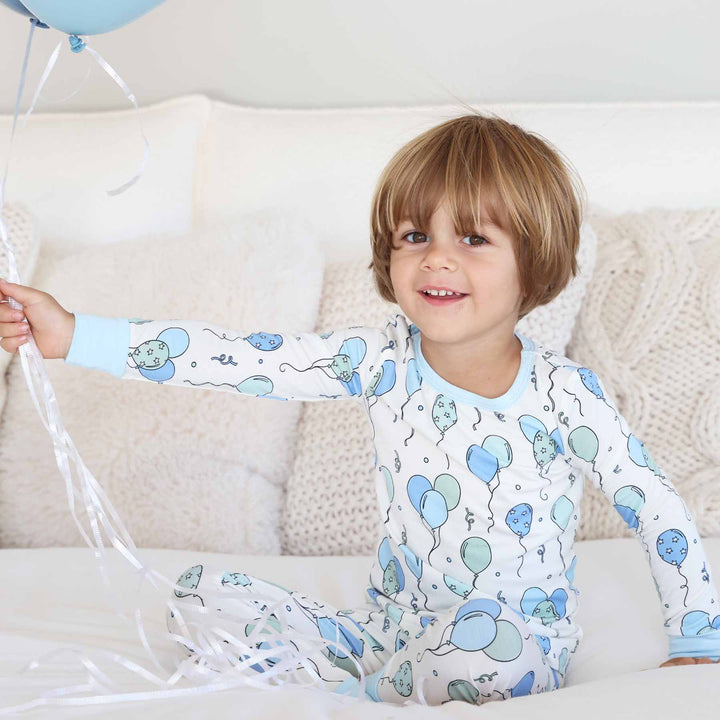 boy holding balloons wearing a blue balloon pajama set 