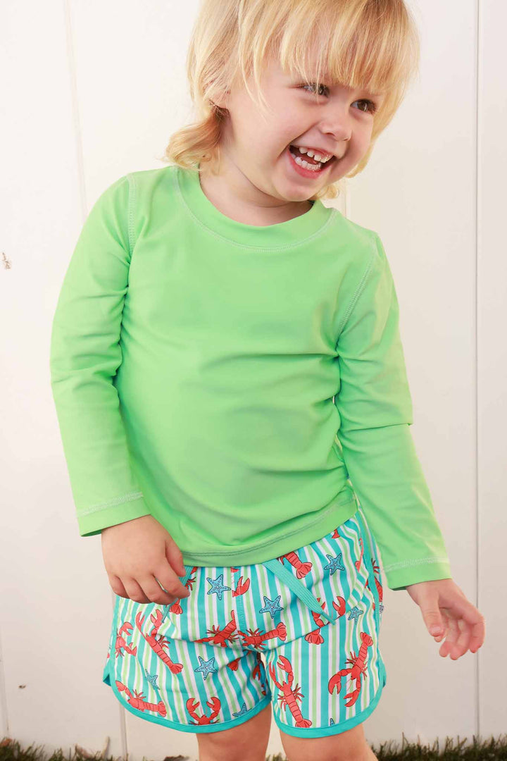 smiling boy in bright green rash guard shirt and lobster swim trunks 