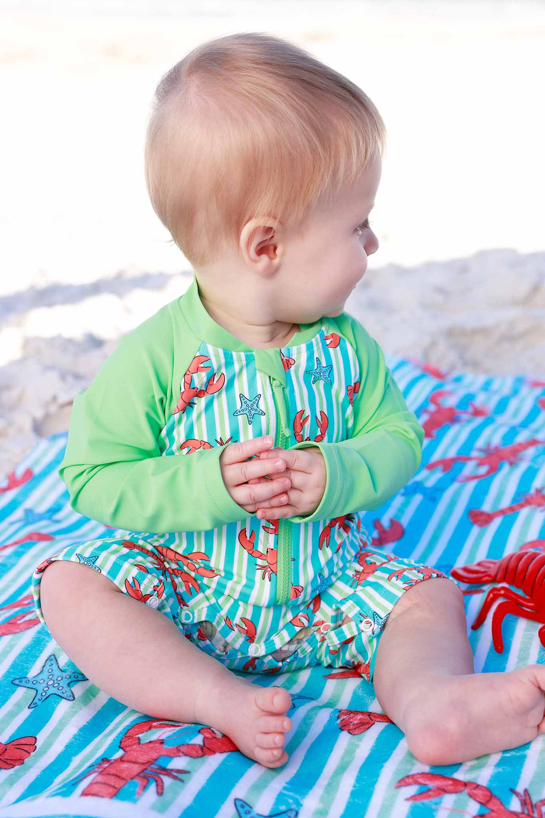 baby boy sitting on beach towel in lobster long sleeve rash guard swim romper shortie