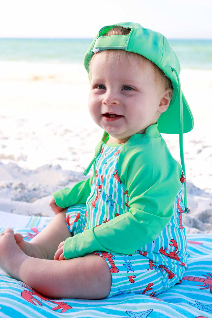 baby boy sitting on beach towel in blue pinch me long sleeve swim romper shortie