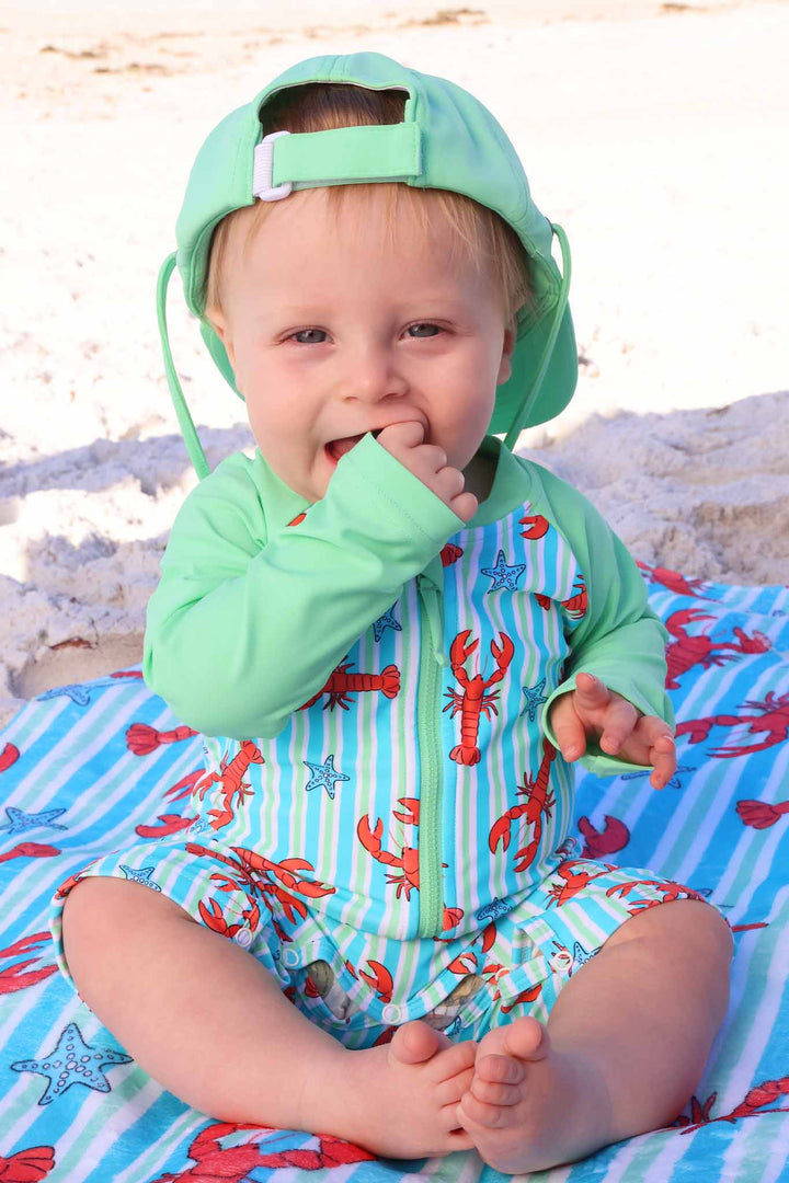 baby boy biting on his finger in lobster long sleeve shortie romper with a matching green surf hat 