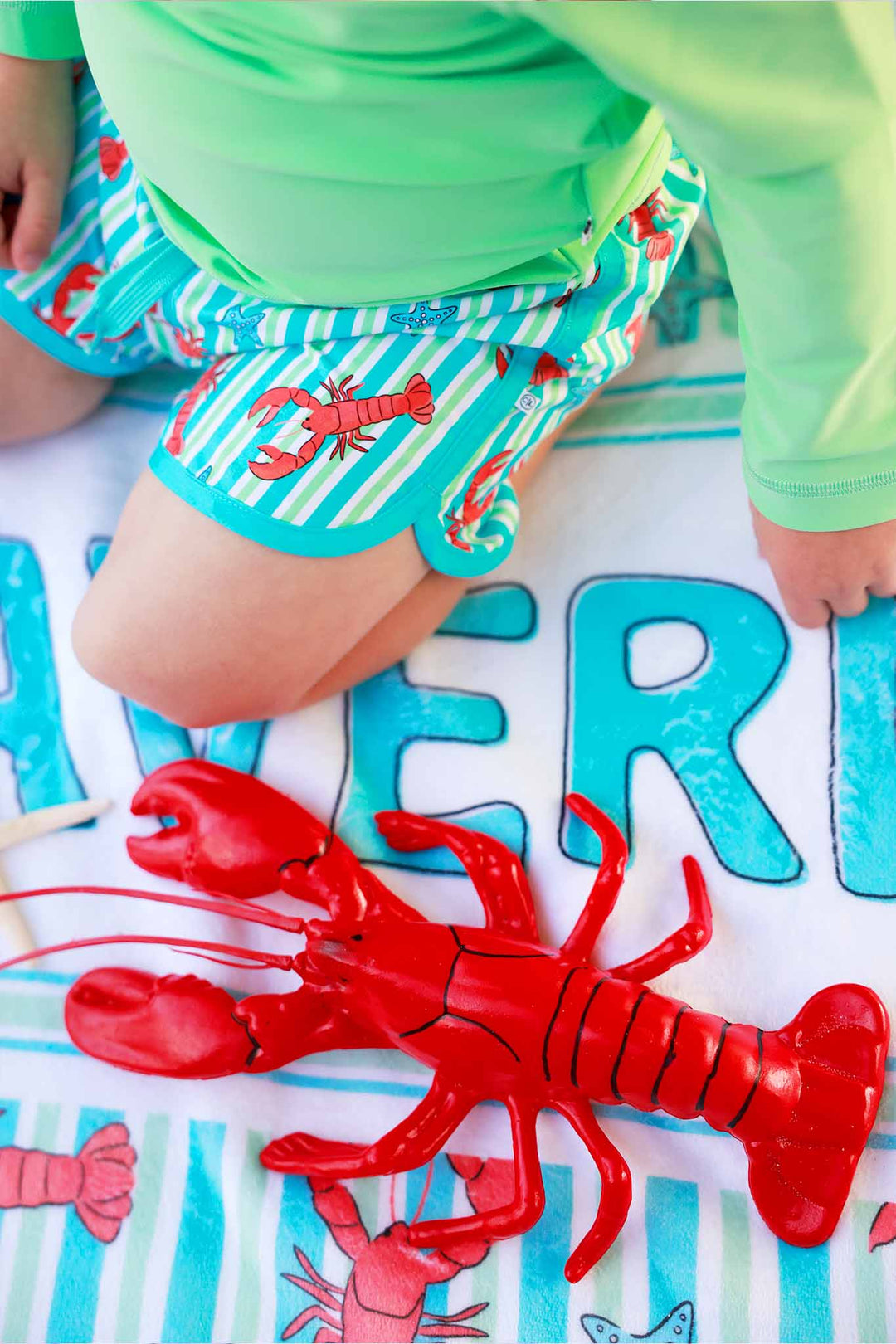 closeup of lobster toy on personalized towel with matching swim trunks 