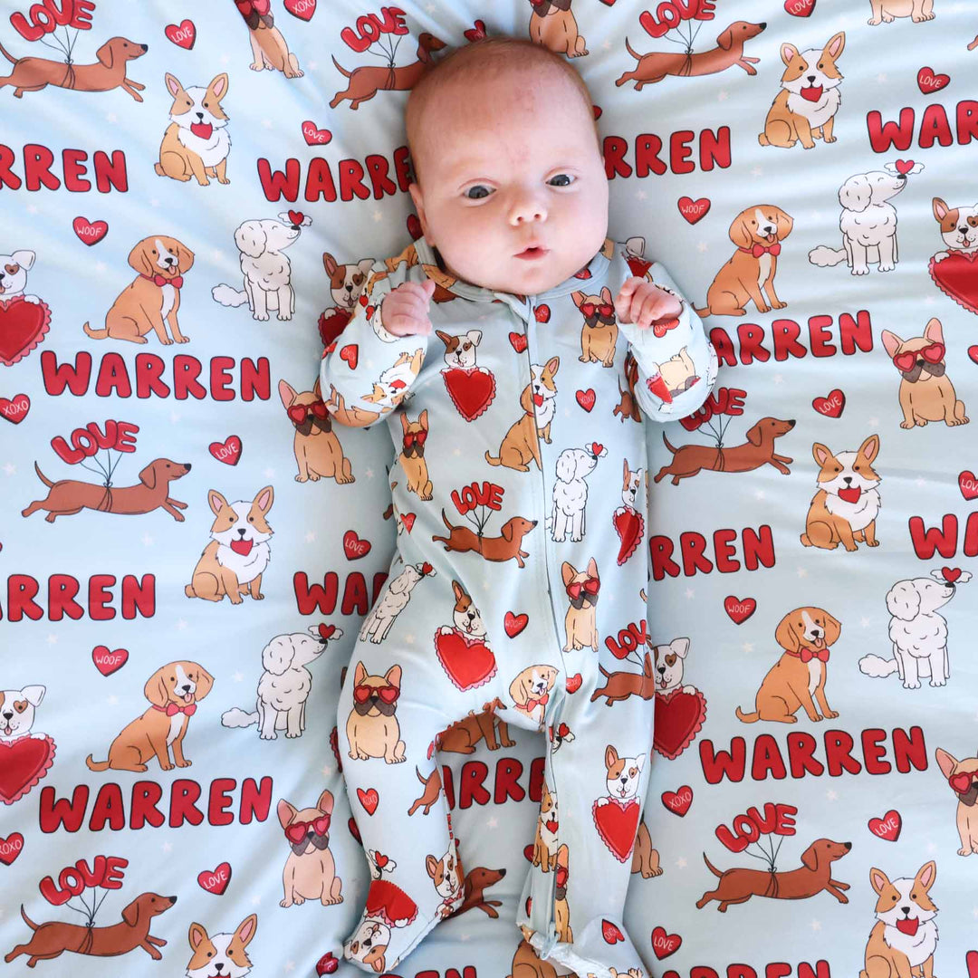 baby boy laying on a personalized swaddle blanket with puppies and hearts for valentine's day in a matching bamboo zipper footie pajama 