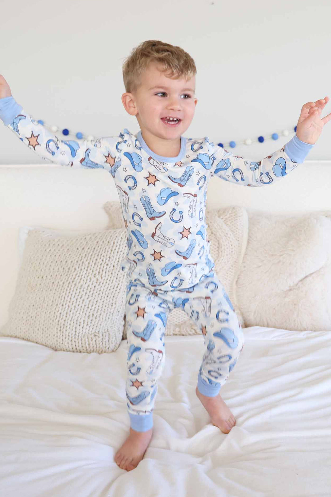 boy jumping on a bed in blue rodeo themed two piece pajama set for kids 