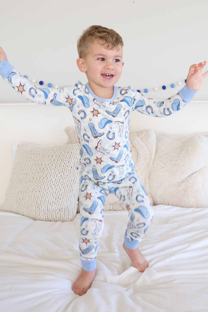 boy jumping on a bed in blue rodeo themed two piece pajama set for kids 