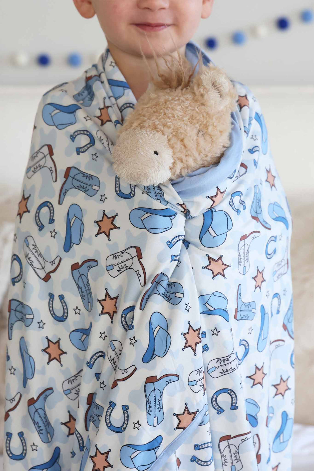 closeup of kids bamboo blanket with blue cowboy hats, boots, horseshoes and sheriff stars 