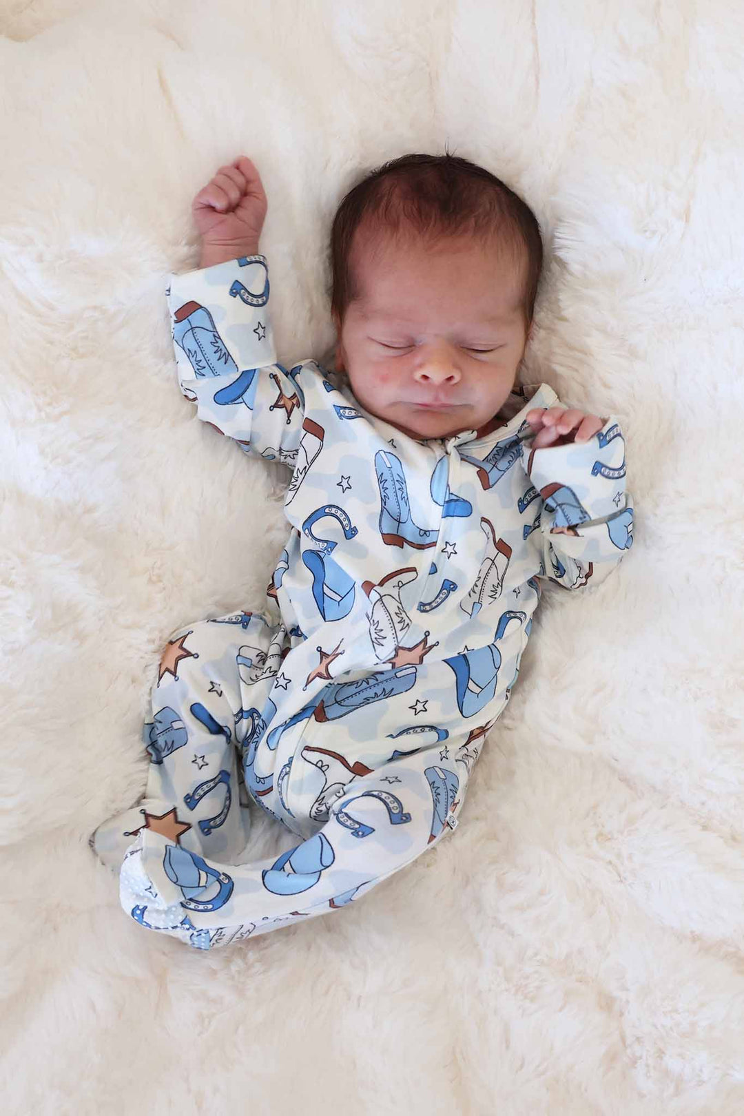 newborn boy laying on blanket wearing blue rodeo themed footie 