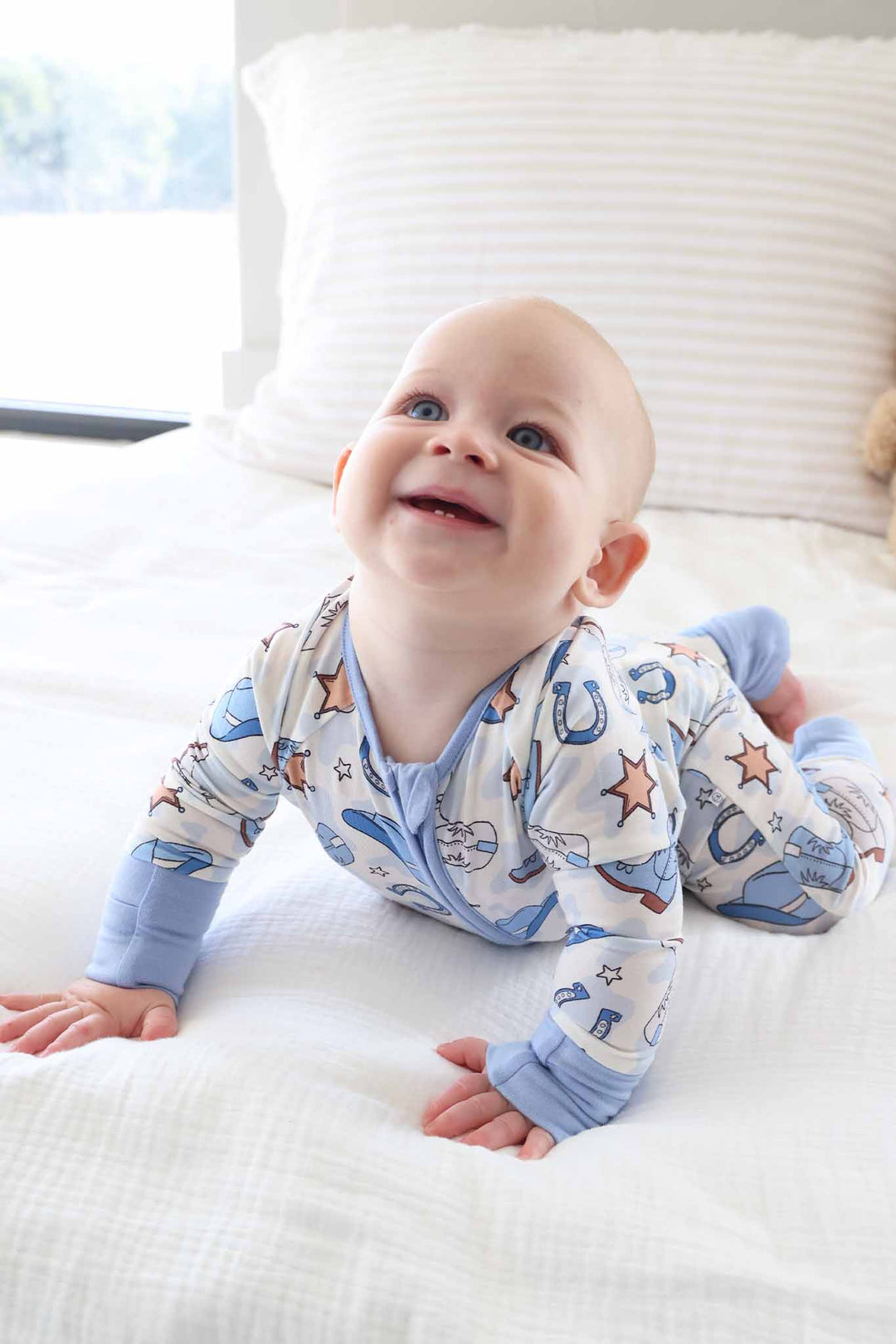smiling baby boy on stomach wearing a western themed pajama in blue 