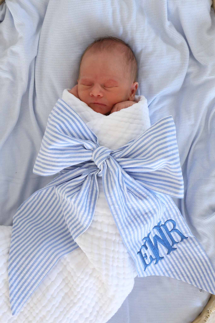 newborn boy wrapped in white gauze swaddle with a blue seersucker bow sash embroidered with monogram