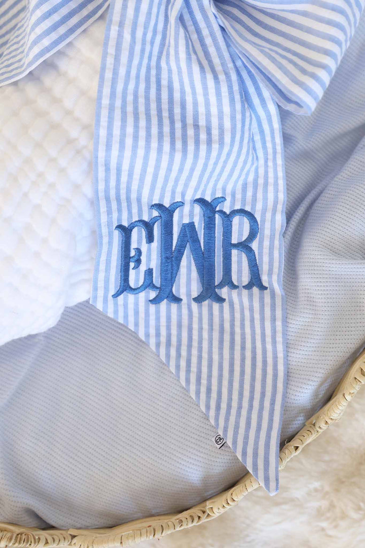 closeup of dusty blue embroidered monogram sash for babies in blue seersucker 