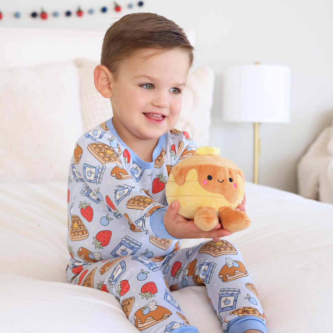 boy wearing blue breakfast themed pajama set holding a pancake stuffed animal 