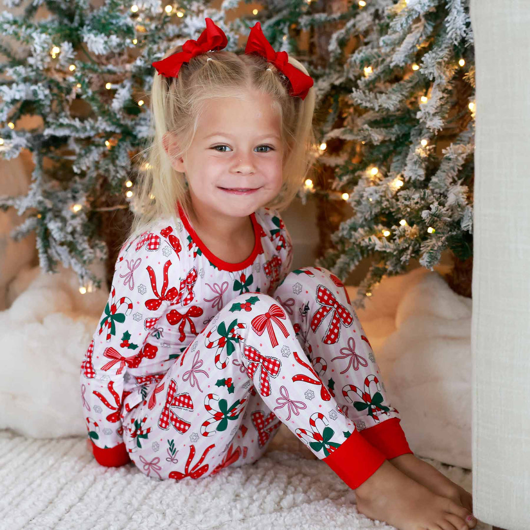 Little girl wearing the Bow What Fun Two Piece Pajama Set while sitting down.
