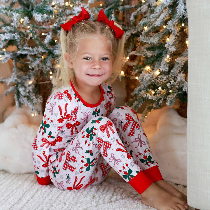 Little girl wearing the Bow What Fun Two Piece Pajama Set while sitting down.