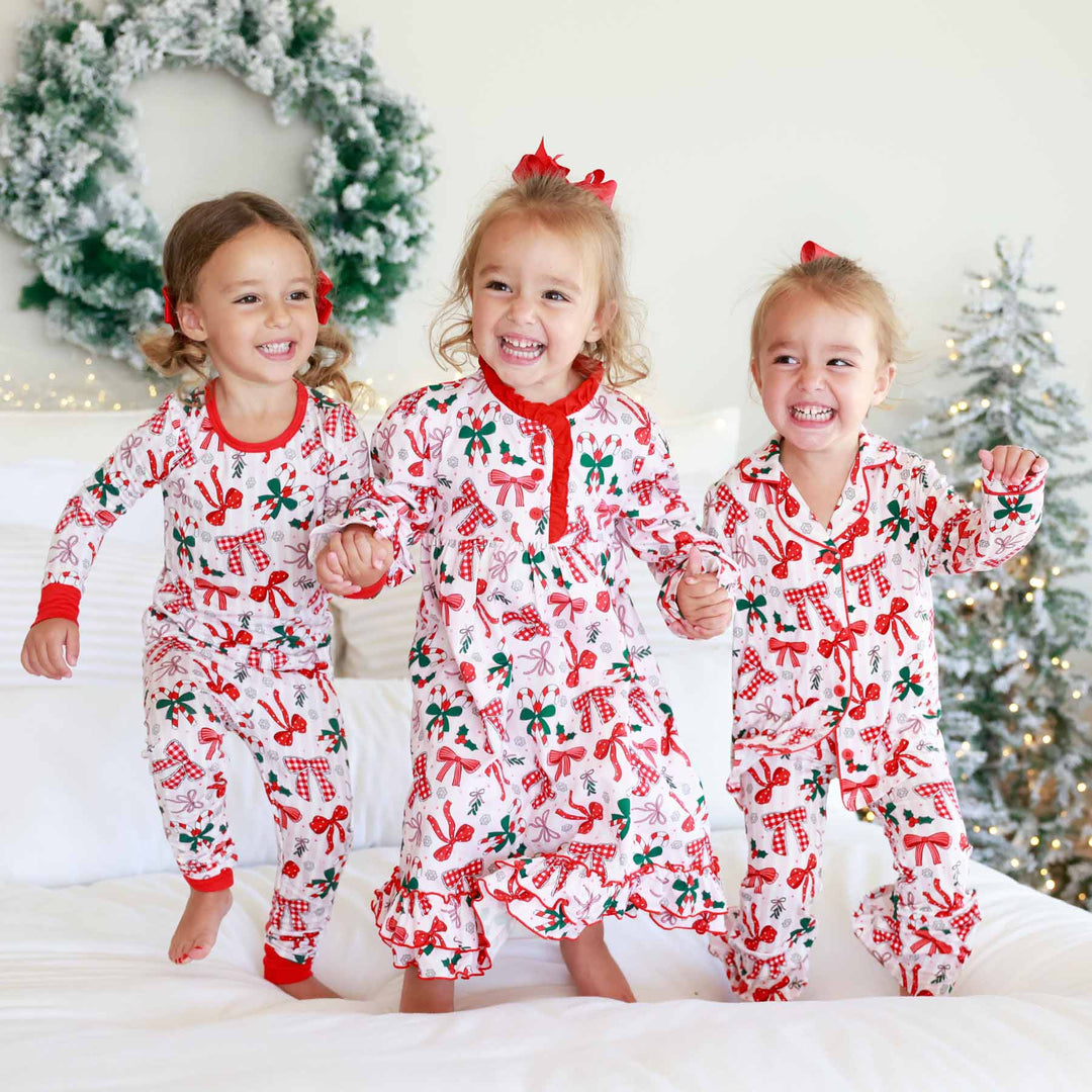 Little girl on the left wearing the Bow What Fun Two Piece Pajama Set. Little girl on the right wearing the Bow What Fun Two Piece Flare Lounge Set while jumping on bed. 