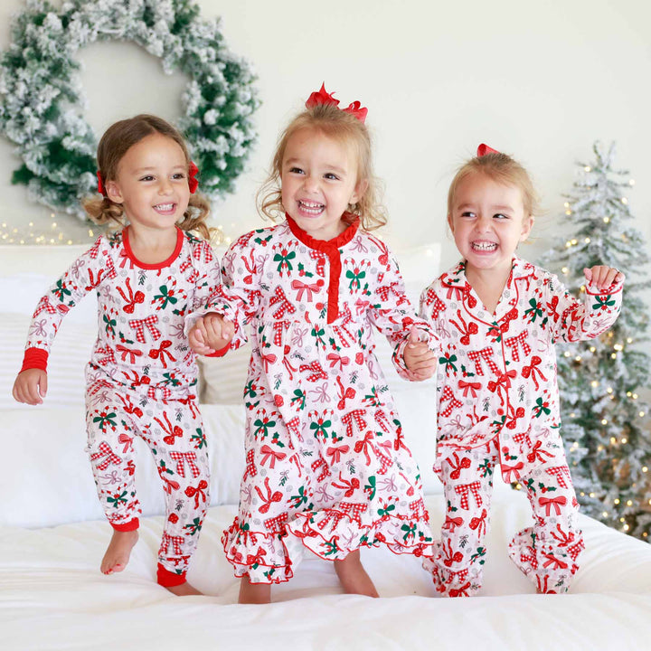 Little girl on the left wearing the Bow What Fun Two Piece Pajama Set. Little girl on the right wearing the Bow What Fun Two Piece Flare Lounge Set while jumping on bed. 