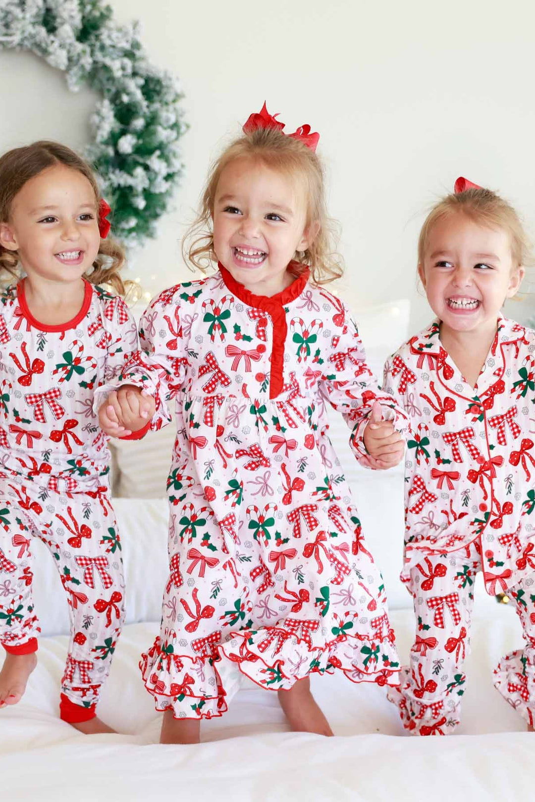 Children wearing a Caden Lane long-sleeve holiday nightgown with a festive bow, candy cane, and holly print