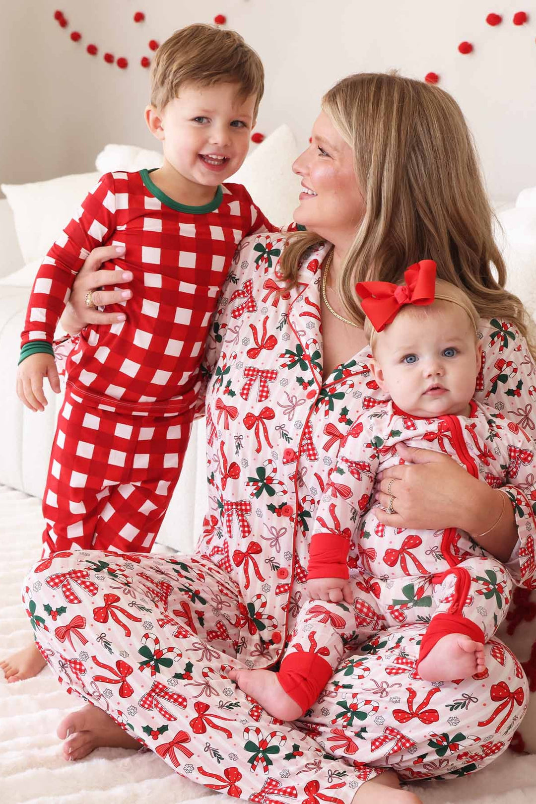 Family in matching Caden Lane holiday pajamas featuring bows, candy canes, holly, and plaid