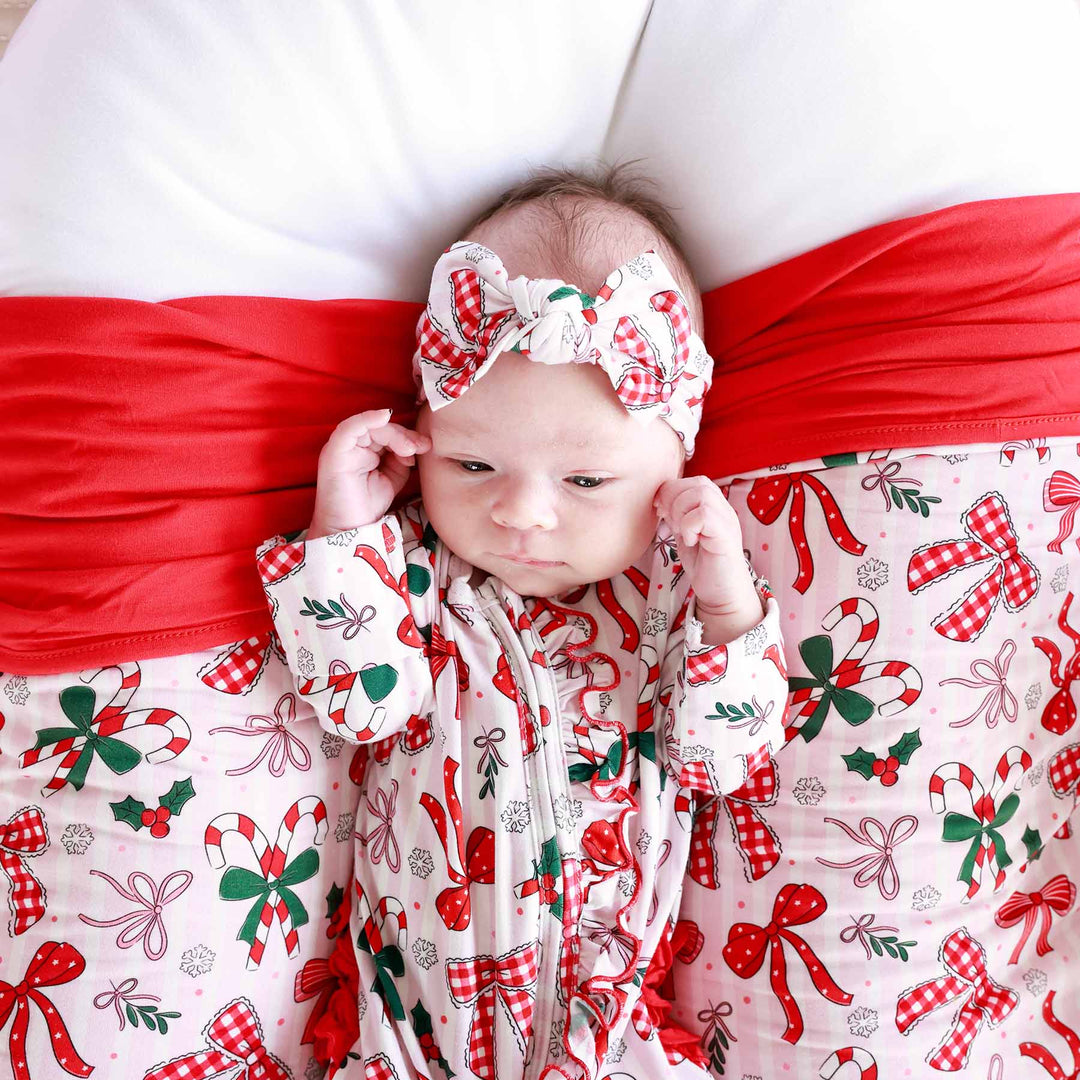 Baby wearing the Bow What Fun Ruffle Zipper Footie with matching bow. 