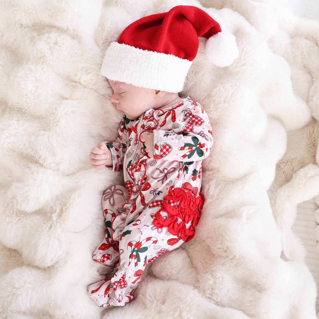 Baby wearing the Bow What Fun Ruffle Zipper Footie with a mini santa hat. 