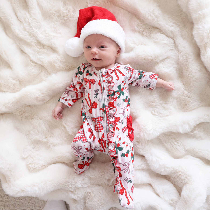 Baby wearing the Bow What Fun Ruffle Zipper Footie with a mini santa hat. 