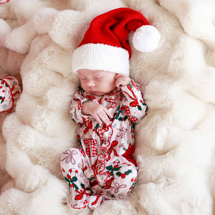 Baby wearing the Bow What Fun Ruffle Zipper Footie with a mini santa hat. 