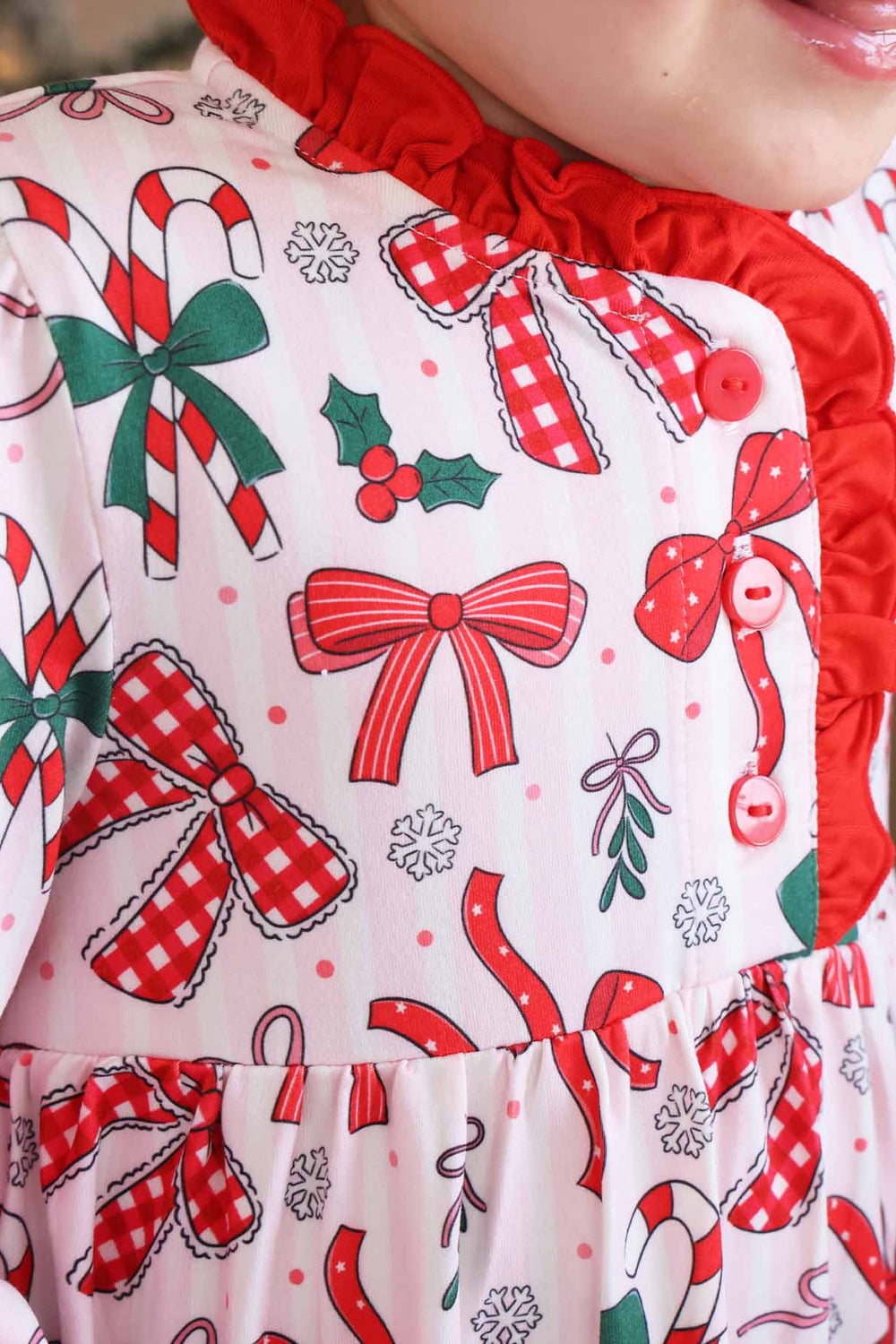 Child wearing a Caden Lane long-sleeve holiday nightgown with a festive bow, candy cane, and holly print