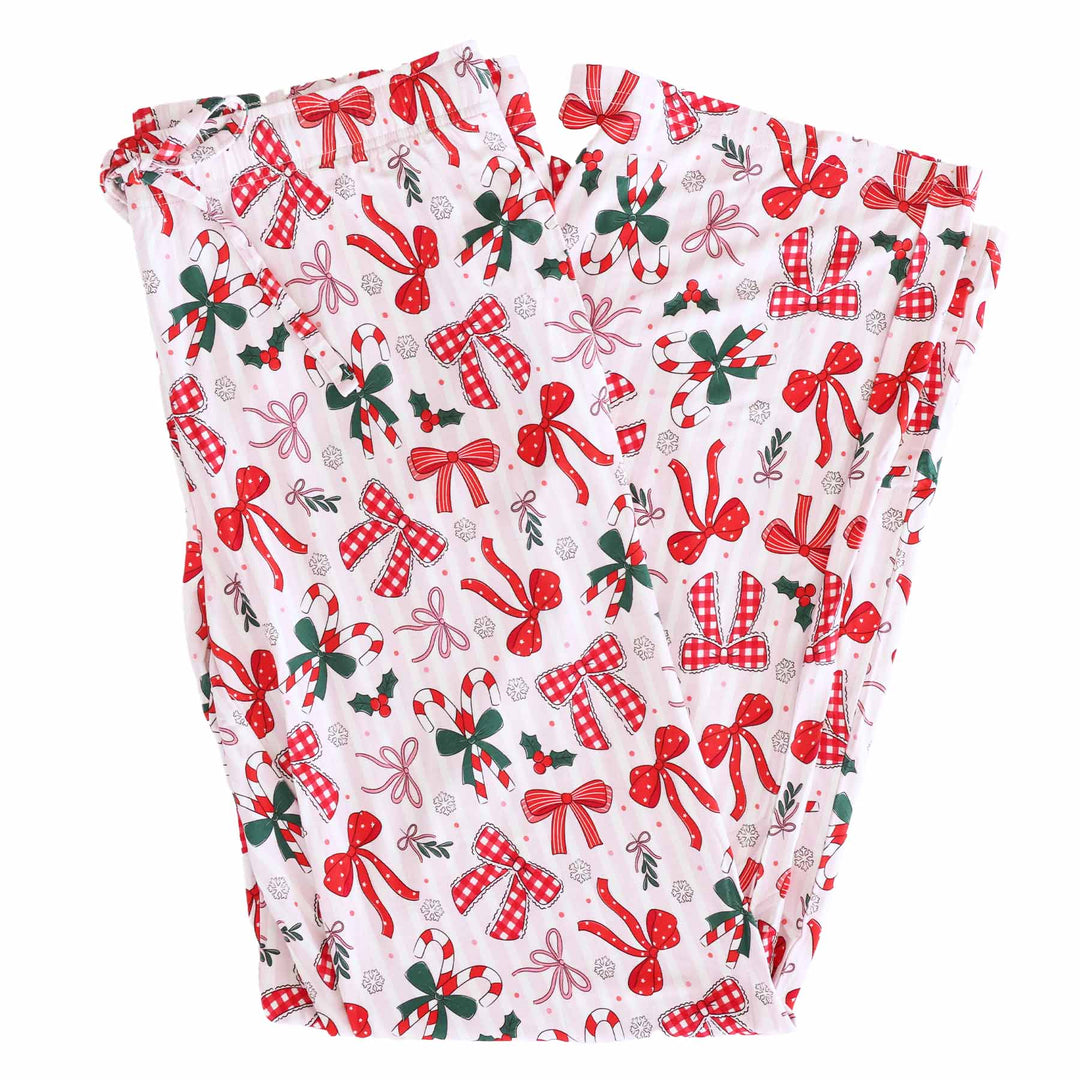 Flat lay of Pajama pants with white and light pink stripes background plus various red bows on top. Unisex Lounge style.