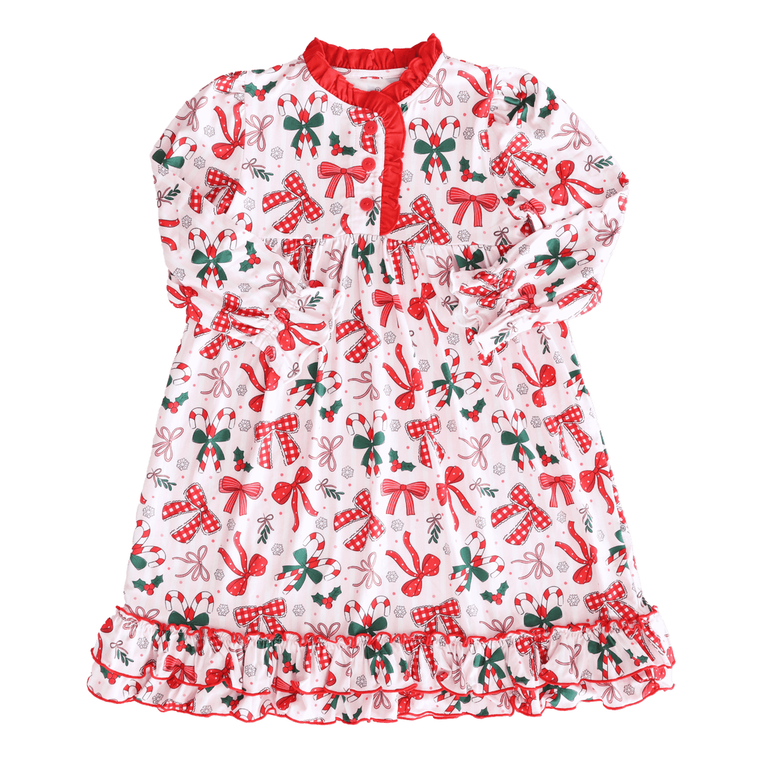Flat lay of a festive girls’ Christmas nightgown with red bows, candy canes, holly, and snowflake print, trimmed with red ruffles.