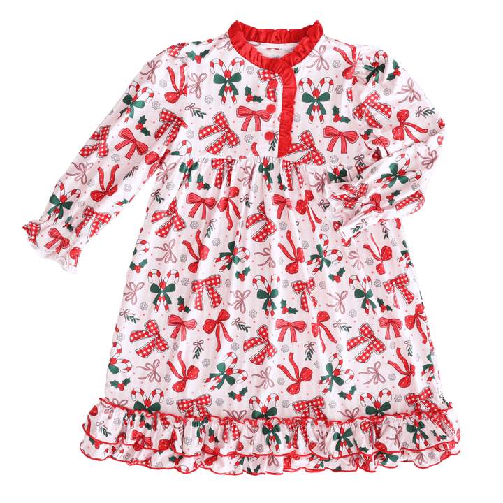 Flat lay of a festive girls’ Christmas nightgown with red bows, candy canes, holly, and snowflake print, trimmed with red ruffles.