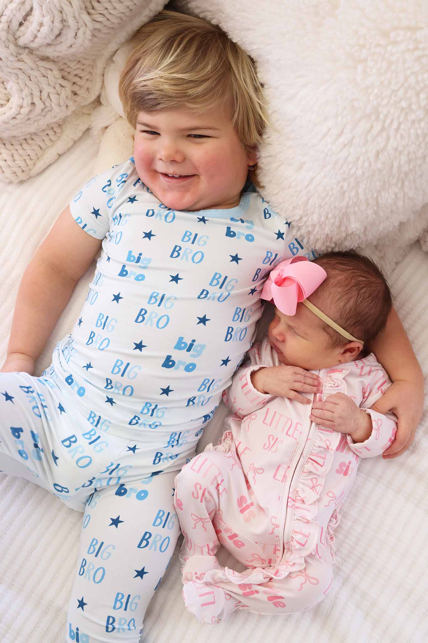 boy wearing big brother two piece pajama set with his arm around his little sister in little sis ruffle zipper footie 