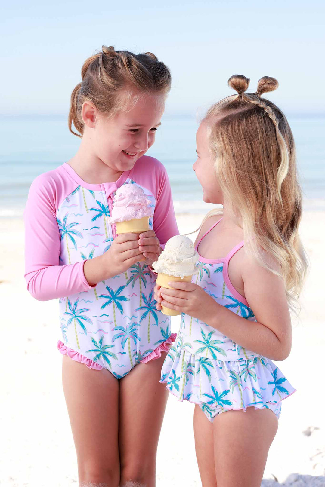 sisters in matching palm tree swimsuits eating icecream on the beach
