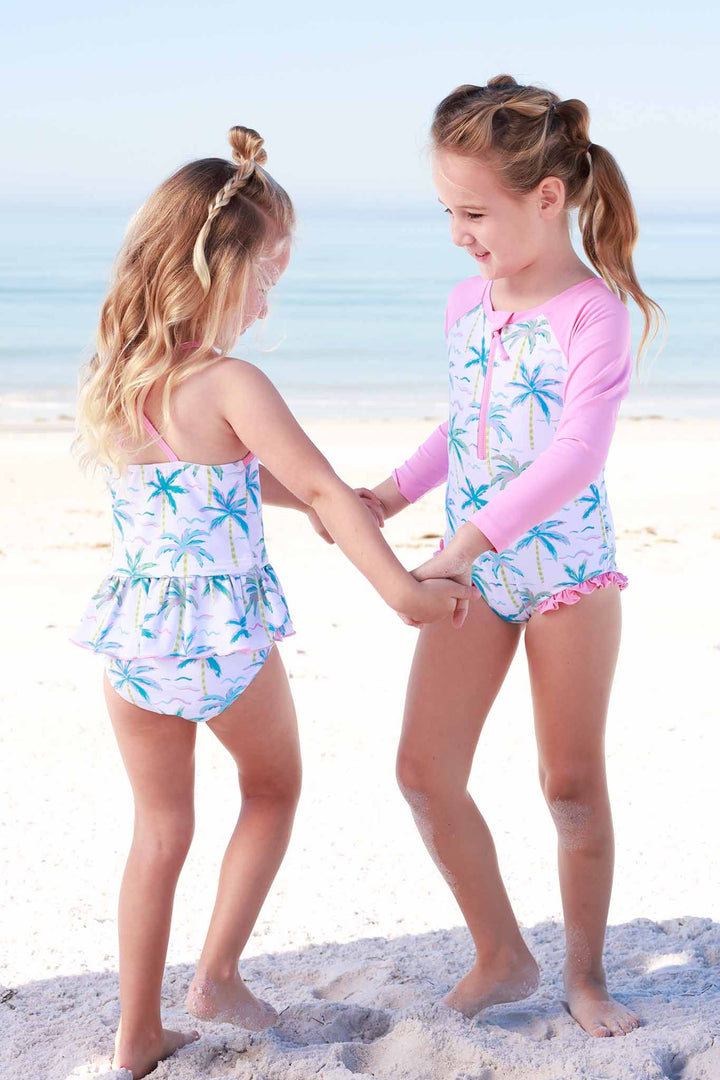 girls wearing coordinating palm tree swimsuits twirling on the beach