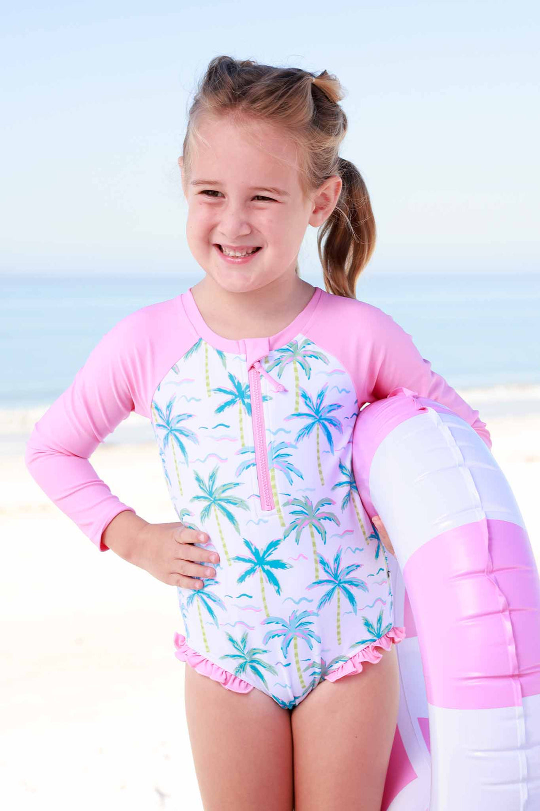 girl standing on beach in neon palm tree rash guard with front zipper with pink long sleeves 