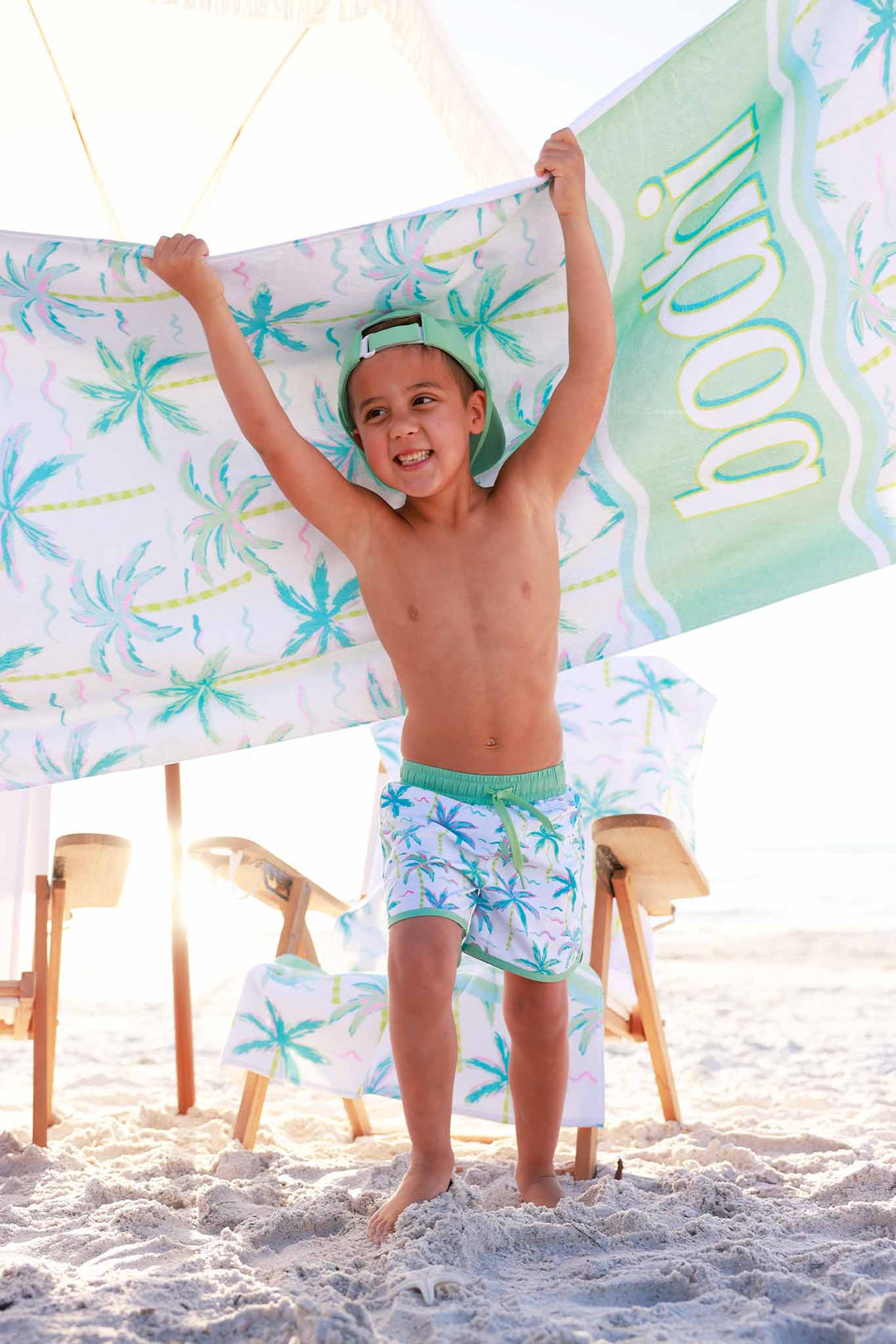 boy running on beach in blue lagoon swim trunks with a personalized beach towel behind him