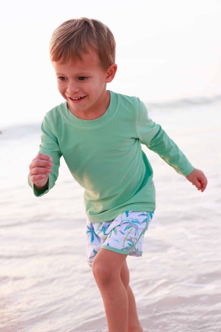 boy running on beach in bright green long sleeve rash guard shirt with matching neon palm tree swim trunks 