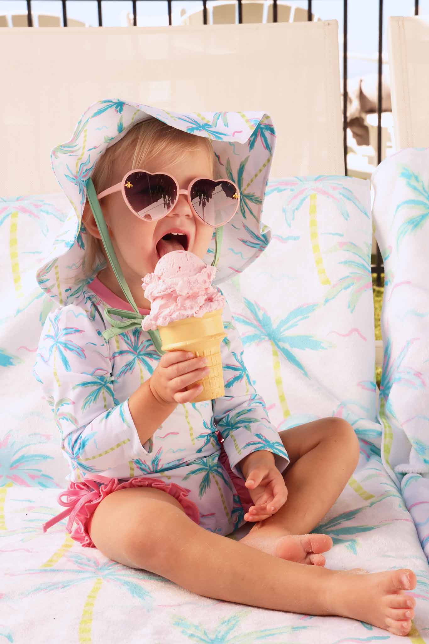 girl eating ice cream wearing blue lagoon rash guard wearing matching hat and sitting on matching towel