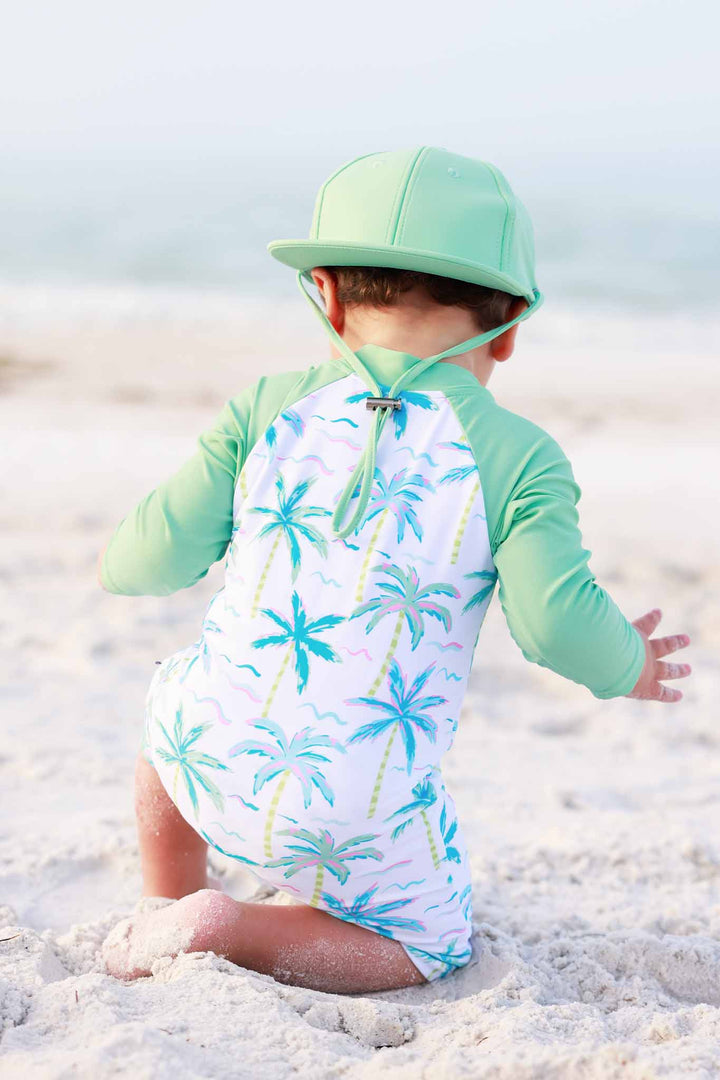 backwards view of palm tree rash guard shortie romper with tropical green surf hat 