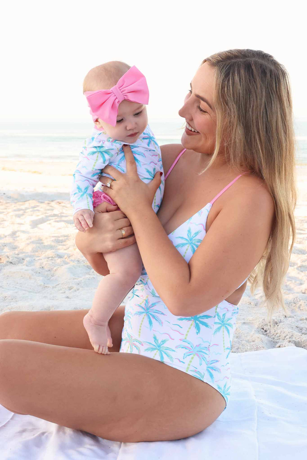 mom wearing blue lagoon cutout swimsuit holding baby girl in matching rash guard swimsuit 
