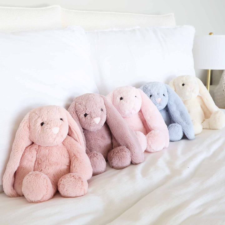 Row of pastel-colored plush bunnies on a white bed