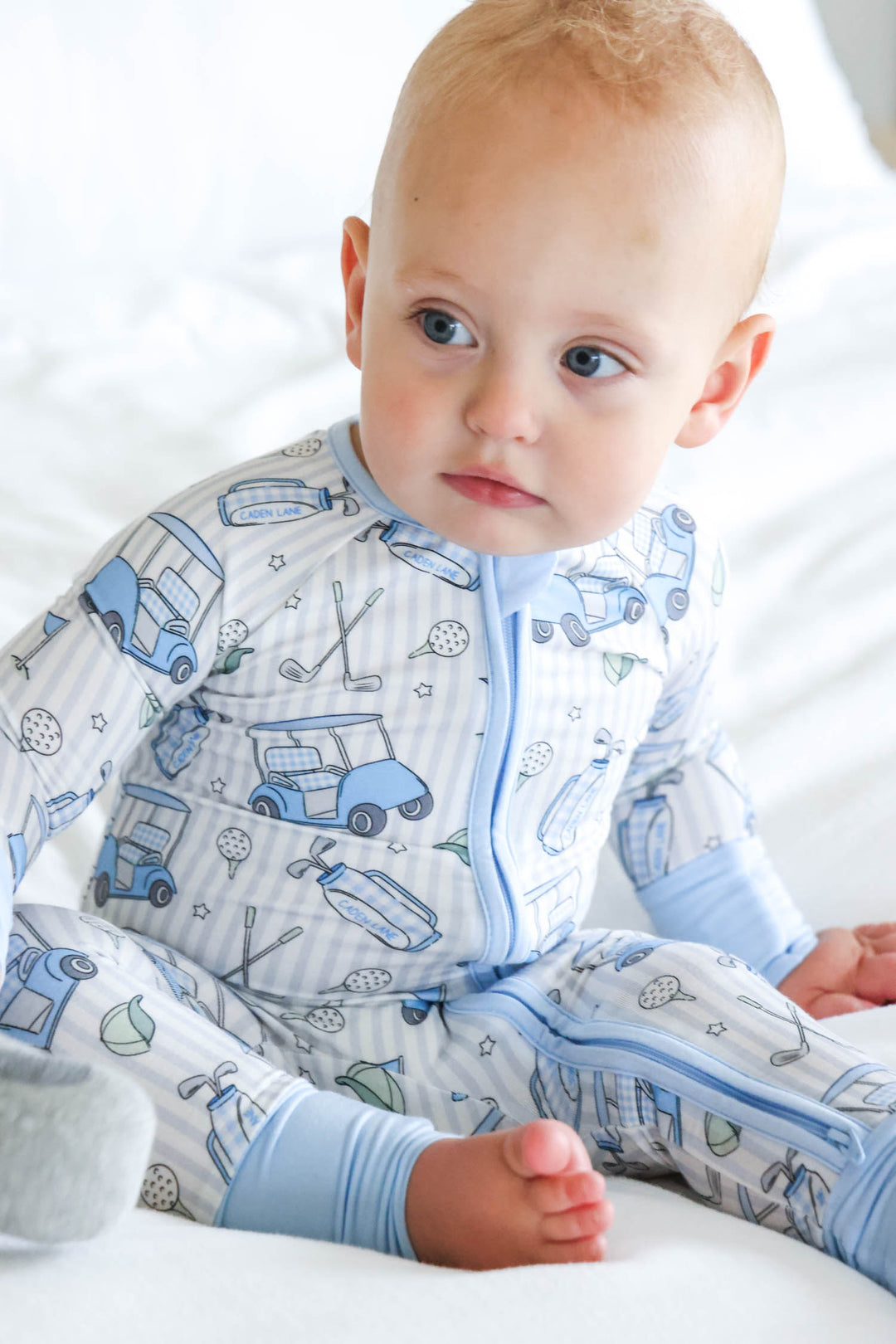 baby boy sitting on bed in caddie crew blue convertible zip romper