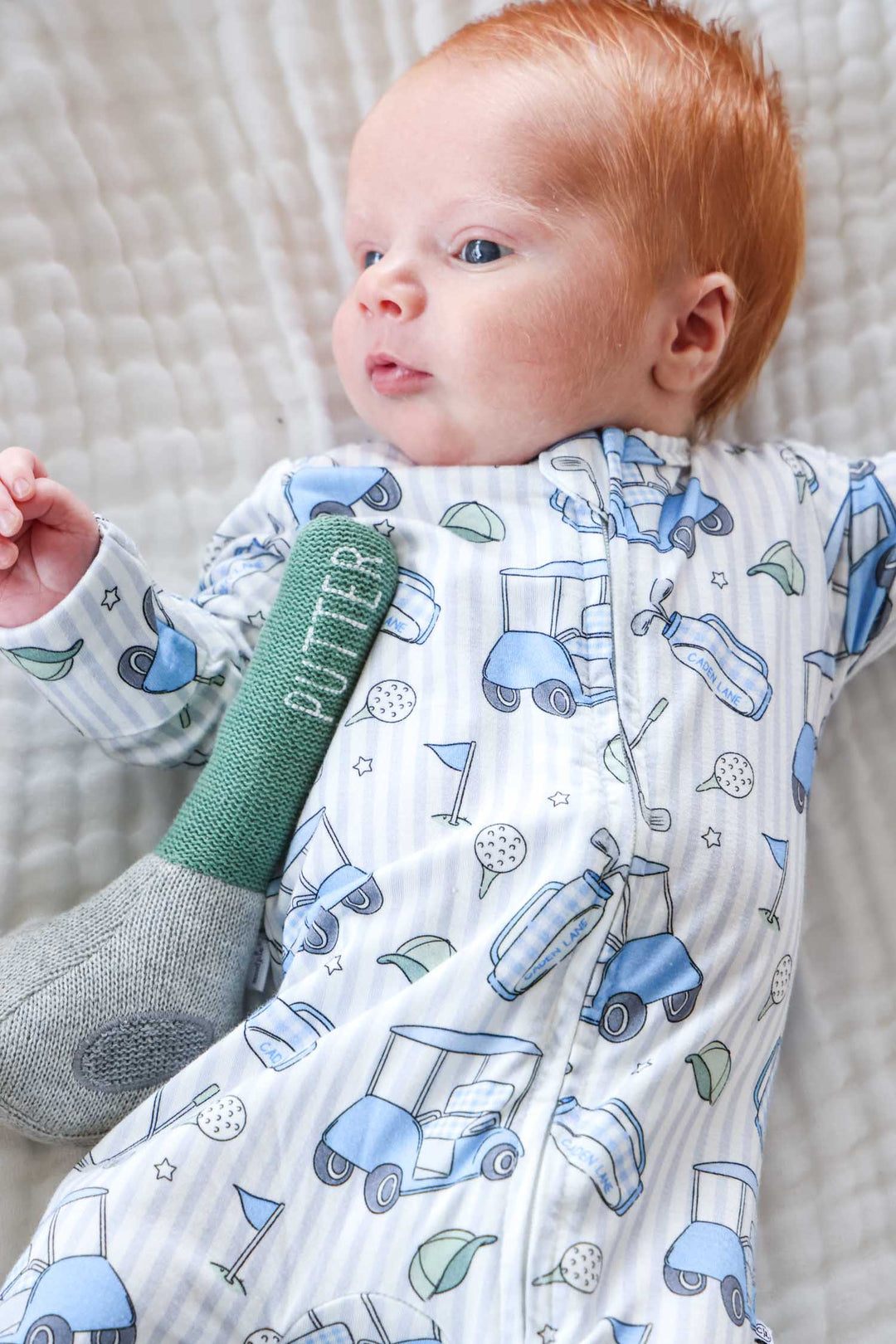 baby boy laying down in blue golf zipper footie with golf club stuffy