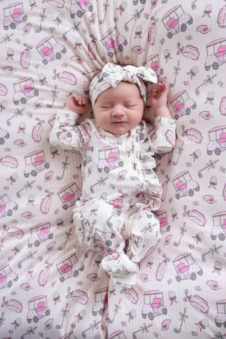 baby girl in pink caddie crew ruffle zipper footie with matching headwrap on bamboo blanket