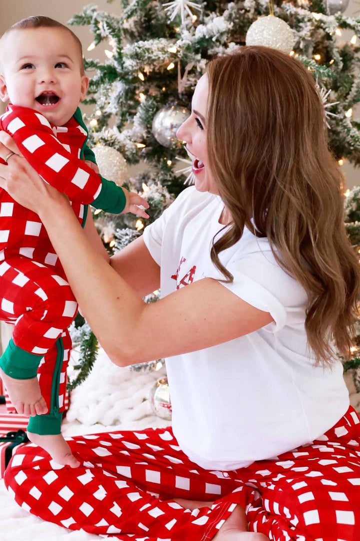 Mother and son wearing matching red and white checkered Christmas pajamas, smiling beside a decorated Christmas tree