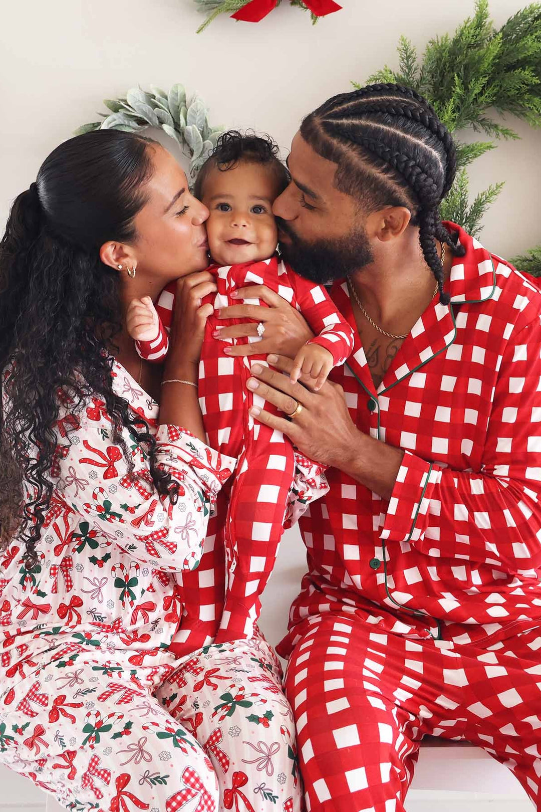 Smiling family wearing coordinating Caden Lane Christmas pajamas, with parents holding their baby in matching red and white checkered holiday sleepwear