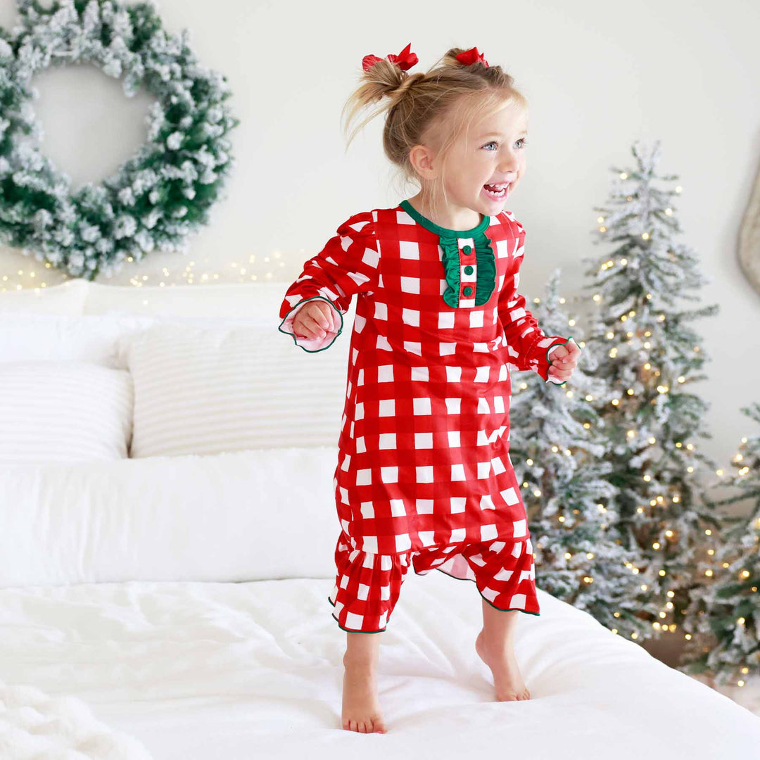 girl wearing red and white check long sleeve full length nightgown with ruffles and buttons jumping on the bed 