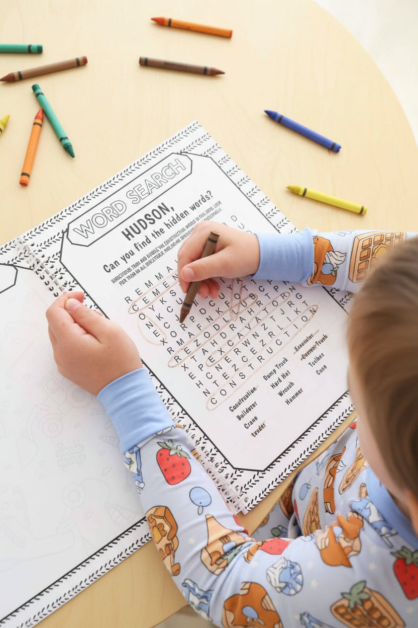 Child circling words with a brown crayon on a personalized 'Hudson' construction word search page in a Caden Lane coloring book