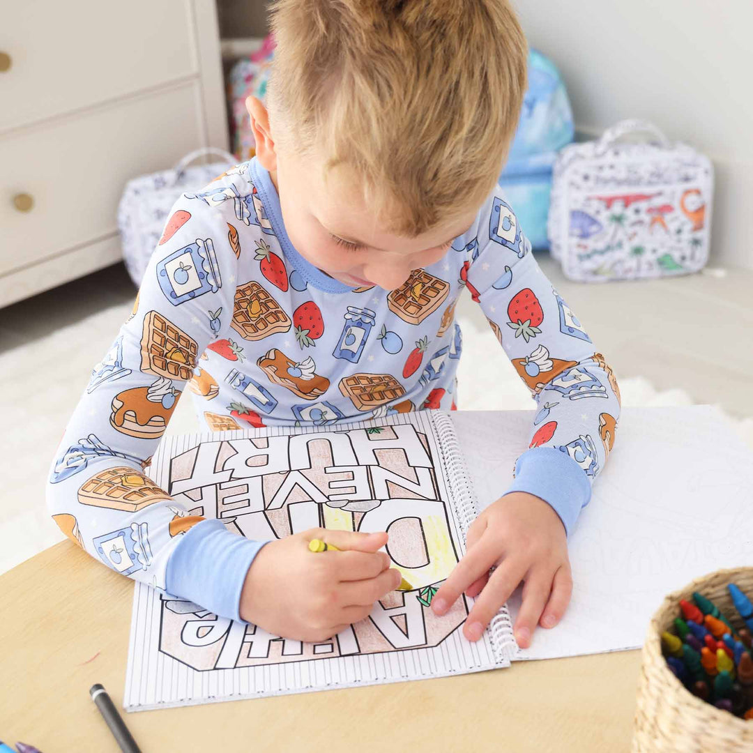 boy wearing breakfast themed pajamas coloring a coloring book that says "a little dirt never hurt"