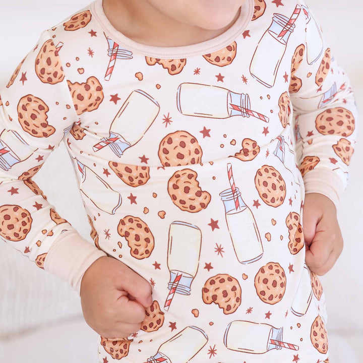 beige pajama set for kids with cookies, jars of milk with a red and white striped straw and black stars
